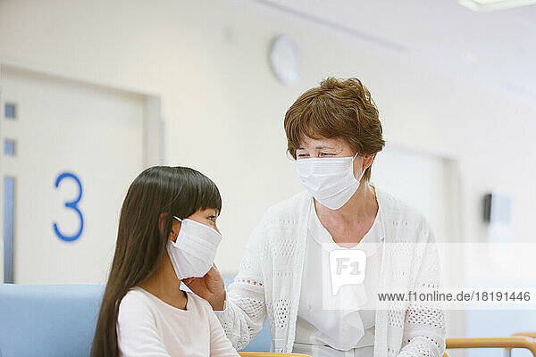 Japanese senior woman and grandchild in masks in hospital waiting room