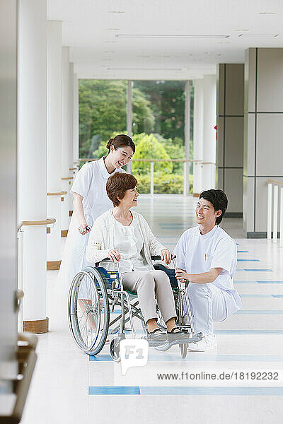 Japanese senior woman in a wheelchair and a two young nurses having a conversation in the hallway