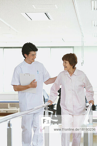 Smiling senior Japanese woman and young male nurse in rehab facility