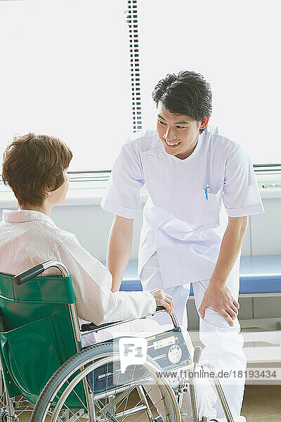 Japanese senior woman in a wheelchair and a young male nurse having a conversation