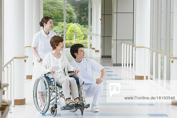 Japanese senior woman in wheelchair and two young nurses in the hallway