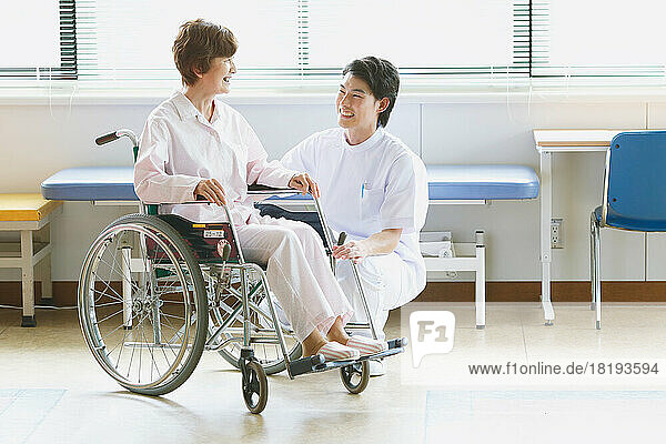 Japanese senior woman in a wheelchair and a young male nurse having a conversation