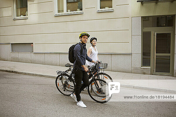 Young man and woman riding bicycles on city street