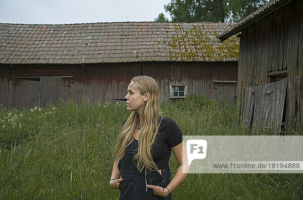 Teenage girl standing in grass by barn