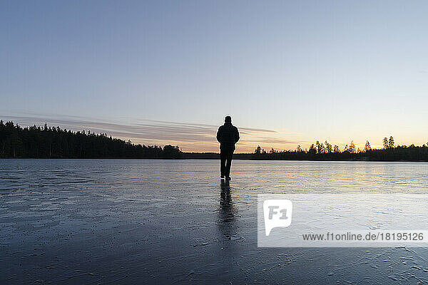 Man walking on frozen lake at sunset