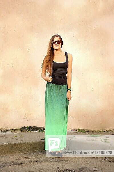 Full length portrait of happy girl in sunglasses  t-shirt and long skirt in front of the wall