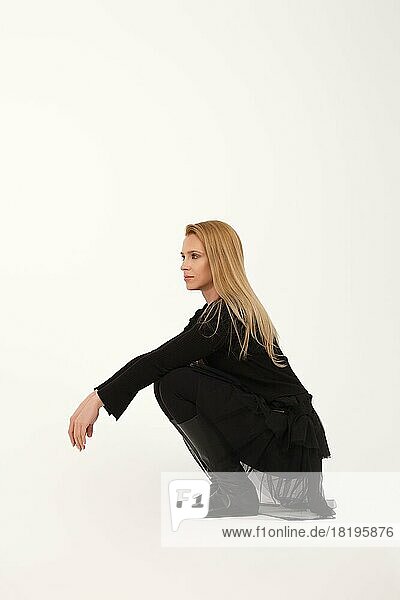 Blonde Dame im Profil sitzend auf ihren Hüften auf hellgrauem Hintergrund