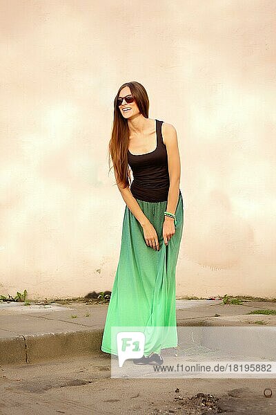 Full length portrait of happy girl in sunglasses  t-shirt and long skirt in front of the wall