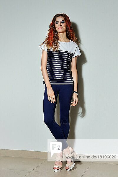 Ganzkörperporträt eines trendigen Hipster-Mädchens mit langen Beinen in engen blauen Hosen  T-Shirt mit Streifen und feuerrot gefärbten Haarsträhnen
