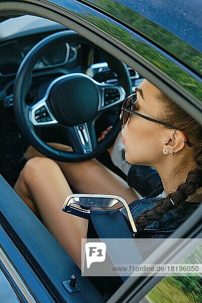 Blick durch die Seitenscheibe eines Autos auf eine Frau  die hinter dem Lenkrad sitzt