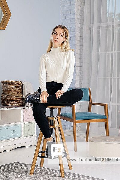 Ganzkörperporträt eines jungen Mädchens auf einem Stuhl im Wohnzimmer sitzend
