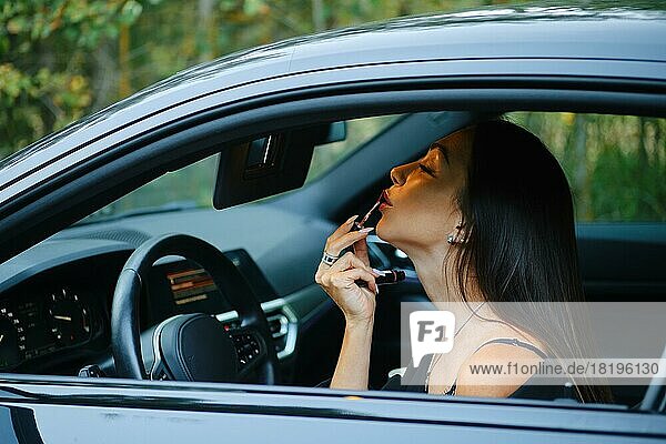 Stilvolle Frau trägt Lippenstift auf  während sie im Auto sitzt