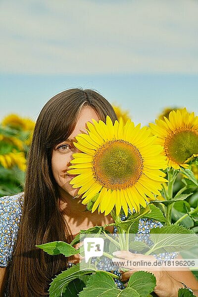 Lustige junge Frau  die ihr halbes Gesicht mit einer Sonnenblume versteckt