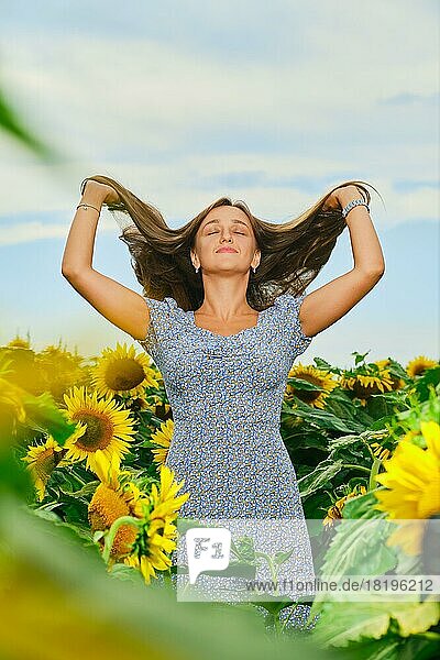 Schöne kaukasische junge Frau hebt lange dunkle Haare in Sonnenblumenfeld