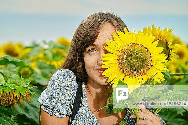 Fröhliche junge Frau  die ihr halbes Gesicht mit einer Sonnenblume verdeckt