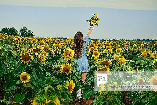 Rückansicht einer Frau mit Sonnenblumenstrauß in der Hand in voller Länge