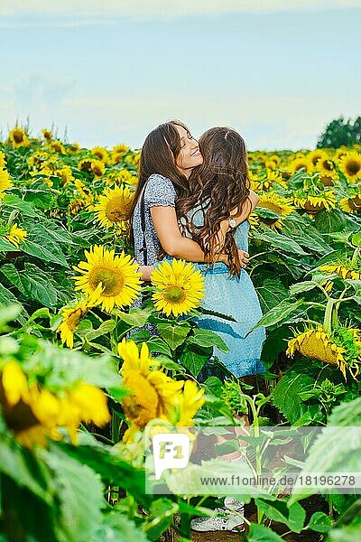 Zwei Freundinnen umarmen sich auf einem Sonnenblumenfeld