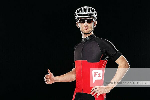 Sport. Radfahrer in Trainingskleidung  Sonnenbrille und Helm zeigt Daumen hoch Zeichen auf schwarzem Hintergrund