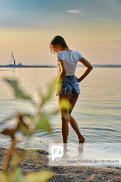 Schöne junge Frau genießt die frische Abendluft am See bei Sonnenuntergang