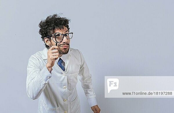 Mad scientist holding a magnifying glass isolated  Man in white coat with magnifying glass looking at camera  Surprised male scientist in lab coat looking at camera with magnifying glass