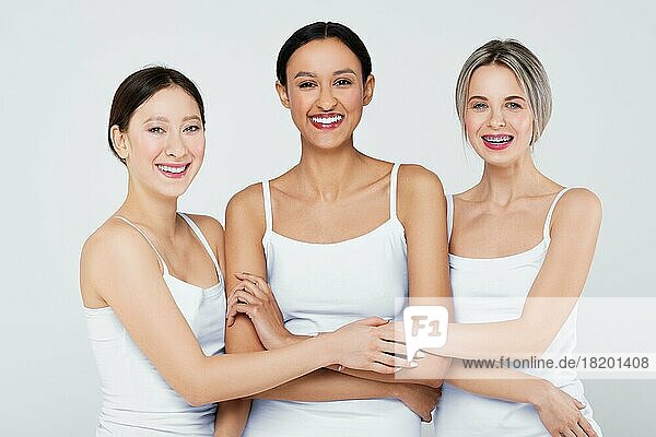 Glückliche asiatische  kaukasische und afrikanische junge Frauen mit verschiedenen Hauttypen in weißen Höschen und Hemd