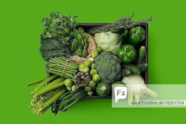 Verschiedene frische grüne Gemüse in Holzkiste auf grünem Hintergrund