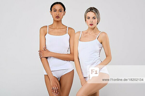 Zwei hübsche kaukasische und afrikanische junge Frauen mit gesunder Haut in weißen Höschen und Hemd