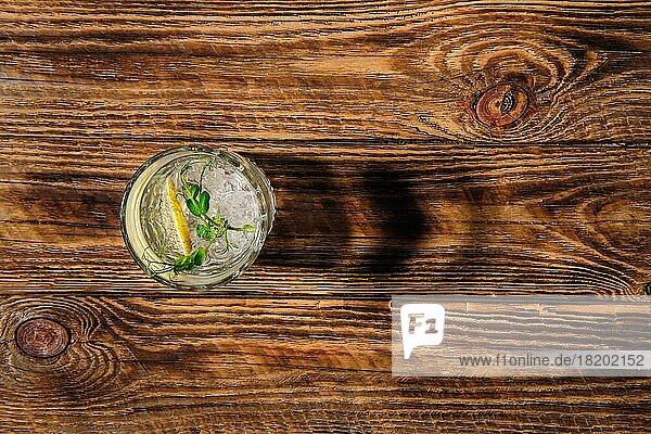 Blick von oben auf ein Glas mit kaltem Wasser mit Eis und Zitrone  das einen Schatten auf einen Holztisch wirft