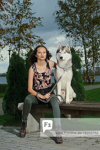 Girl sitting with husky dog in city park. Dog on a bench