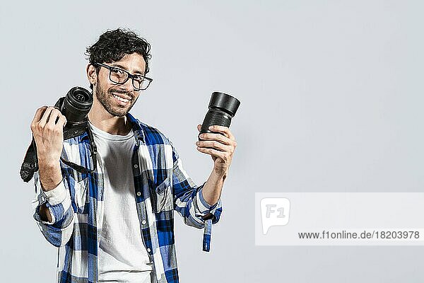 Portrait of smiling photographer man showing a camera and lens on isolated background. Smiling young man holding a camera isolated  Smiling photographer guy showing a camera and lens