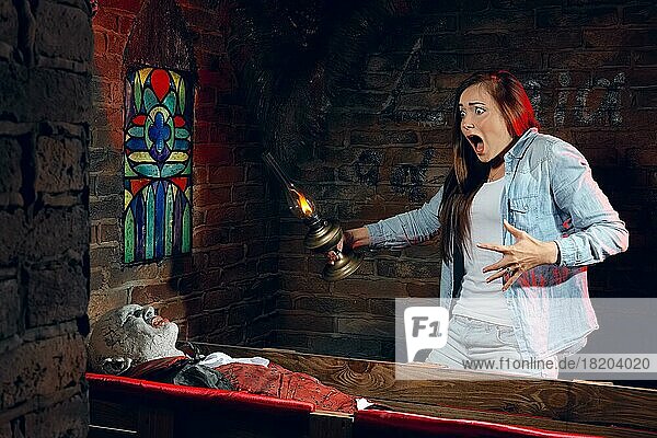 Verängstigte junge Frau mit Lampe in der Hand schreit  als sie einen Sarg mit einem Vampir sieht