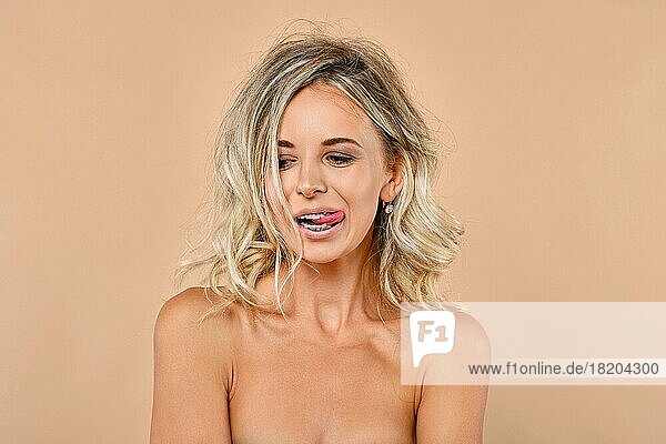 Trickreiche junge Frau mit wilden Haaren und Zahnspange streckt ihre Zunge heraus
