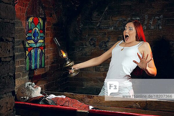 Verängstigte junge Frau mit Lampe in der Hand schreit  als sie einen Sarg mit einem Vampir sieht
