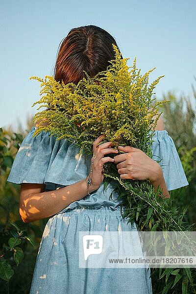 Hübsches Mädchen versteckt Gesicht in Feld mit Blumen