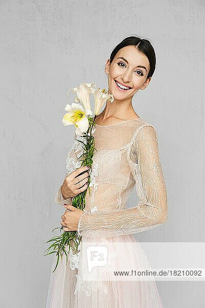 Hübsche junge Frau in transparentem Tüllkleid mit Spitze posiert mit Blumen in der Hand