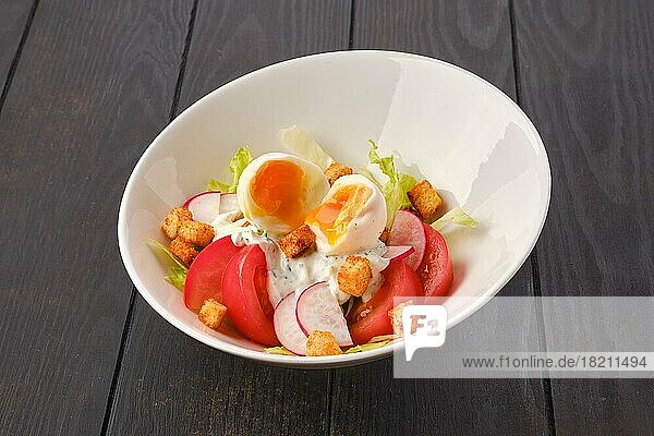 Salat mit frischer Tomate  Radieschen  gekochtem Ei und Crouton auf dunklem Holztisch