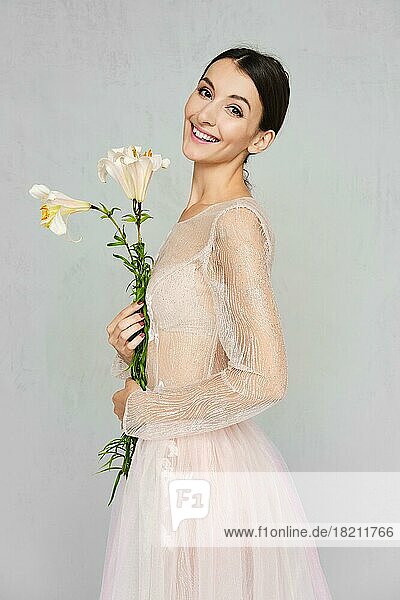 Hübsche junge Frau in transparentem Tüllkleid mit Spitze posiert mit Blumen in der Hand