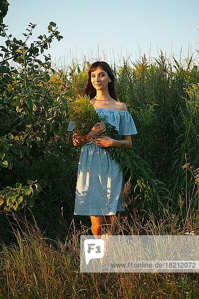 Lustiges Mädchen in himmelblauem Kleid mit Strauß Feldblumen im Sonnenuntergang
