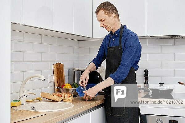 Ein Mann mittleren Alters schlägt ein Ei mit einem Schneebesen auf  um ein Omelett zu machen
