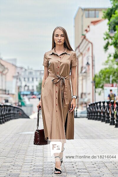 Beautiful happy woman in long olive dress walking on the street of downtown