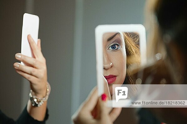 Hübsche junge Frau schaut in einen kleinen Spiegel. Blick über die Schulter
