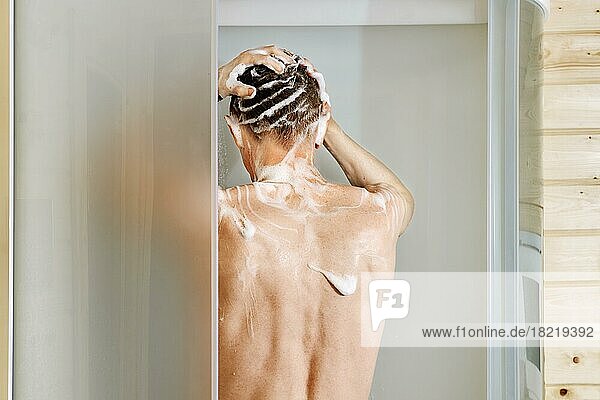 Rückenansicht eines Mannes beim Haarewaschen unter der Dusche