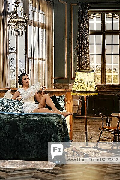 Altmodisches Foto einer attraktiven Frau in Retro-Dessous  die mit einer Feder in der Hand im Bett sitzt