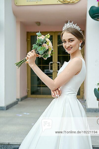 Porträt der schönen Braut mit Krönchen hält Blumenstrauß in den Händen im Freien