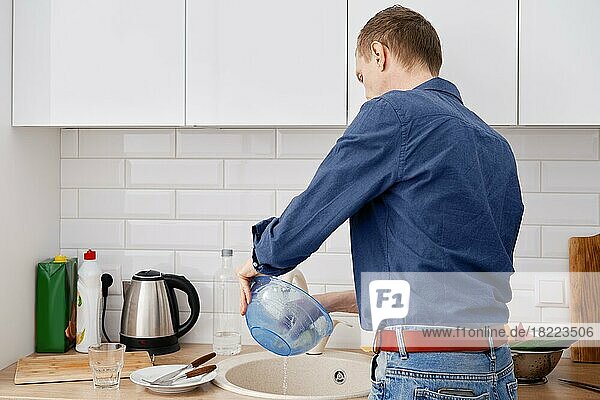 Rückenansicht eines Mannes mittleren Alters wäscht das Geschirr nach dem Kochen zu Hause