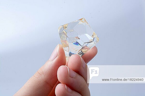 Hand hält einen transparenten Diamanten auf weißem Hintergrund