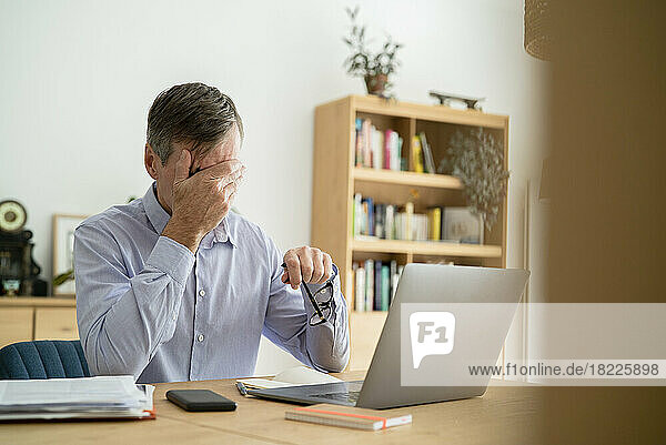 Stressed senior businessman with hand on face doing home office