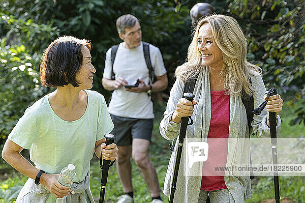 Two middle-aged ladies with hiking poles walking in the woods with their partners behind them