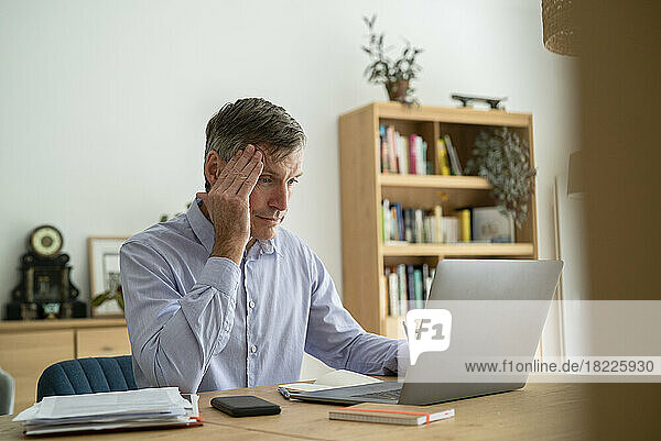 Senior businessman having a headache while using laptop at home