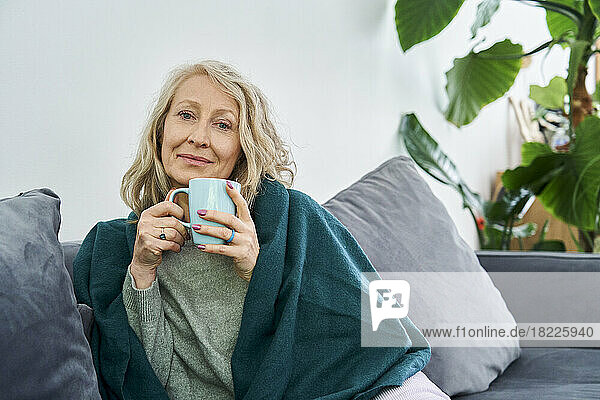 Senior woman sitting on couch while holding cup of tea